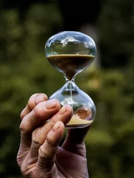 Close-up of an hourglass held by a hand, symbolizing time in a natural setting.